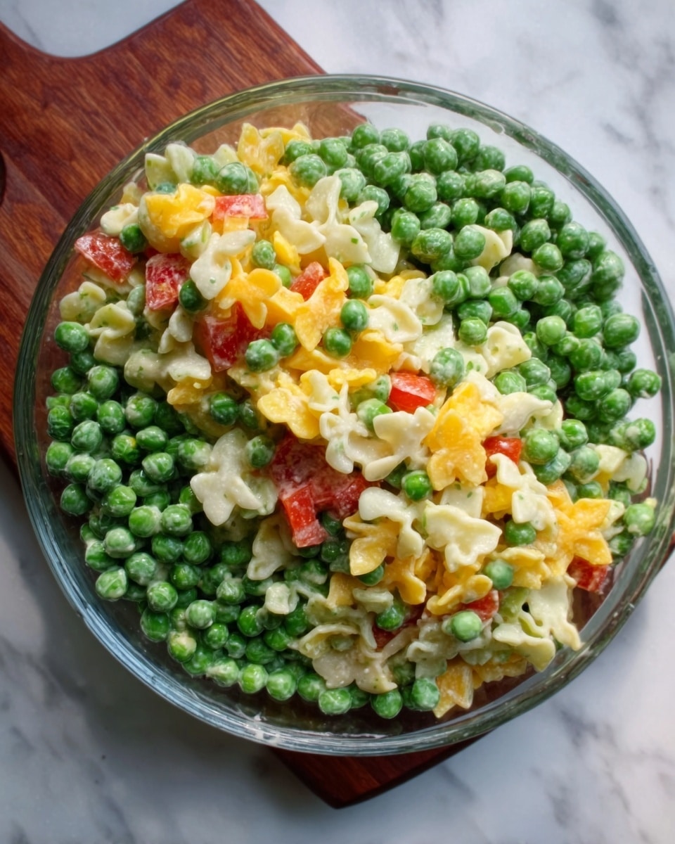 A clear glass bowl filled with three main layers of colorful food sits on a white marbled surface. The bottom layer is made of bright green peas that add a fresh and round texture. Above the peas, there is a layer of yellow and white pasta shaped like flowers, giving a light and soft look. Scattered throughout the pasta are small pieces of red tomatoes, adding a pop of color and soft texture. The dish looks fresh and colorful with a mix of green, yellow, white, and red. photo taken with an iphone --ar 4:5 --v 7