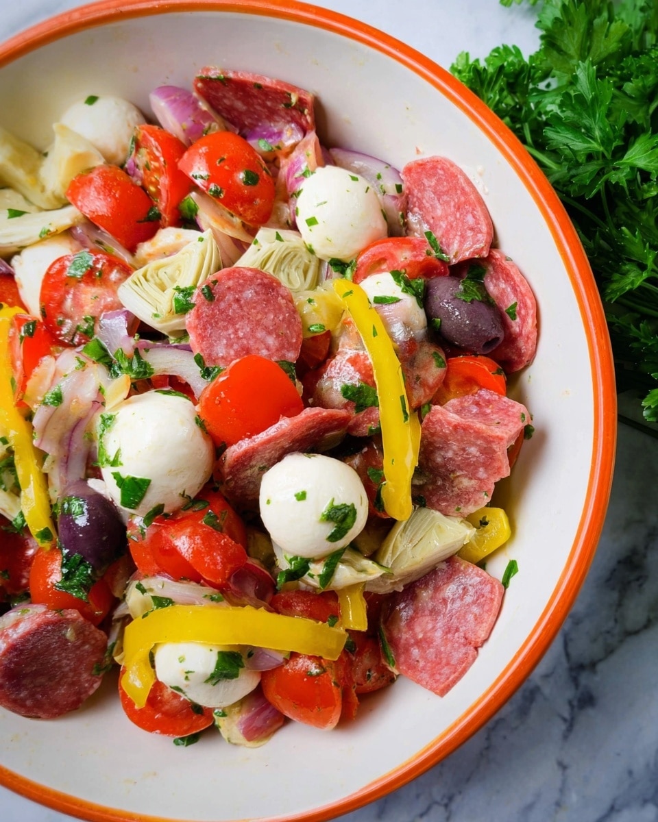This image shows a close-up of a salad served in a white bowl with an orange rim, placed on a white marbled surface with some fresh parsley in the background. The salad has multiple layers and colors; the bottom layer consists of green parsley leaves scattered throughout. Above that are round white mozzarella balls, halved and whole. Bright red cherry tomatoes are mixed in, some whole and some halved, adding vibrant color. There are also thin slices of pink salami and red pepperoni, cut into small square and triangular shapes, giving a textured look. Thin rings and strips of yellow banana peppers spread through the bowl, adding bright yellow accents. Dark purple olives and small off-white artichoke hearts are spread evenly. The salad is lightly coated with a glossy dressing that adds a fresh shine to everything. photo taken with an iphone --ar 4:5 --v 7
