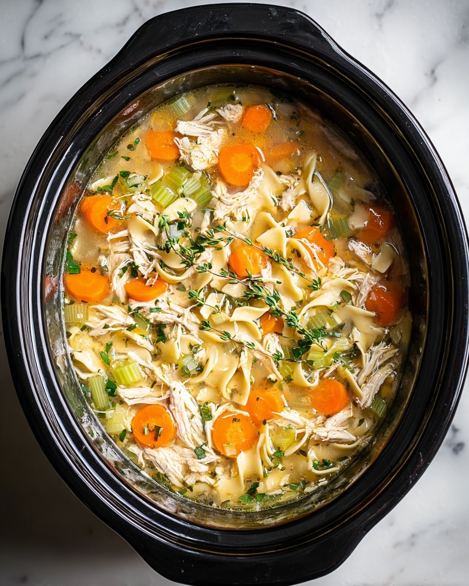 A black slow cooker filled with chicken noodle soup is shown from above. The soup has visible layers including shredded white chicken pieces scattered evenly, orange carrot slices, light green celery chunks, and small, pale yellow egg noodles floating in a clear broth. Fresh green herb sprigs are laid on top, adding a touch of color and freshness. The edges of the slow cooker frame the soup within, set on a white marbled texture surface. photo taken with an iphone --ar 4:5 --v 7