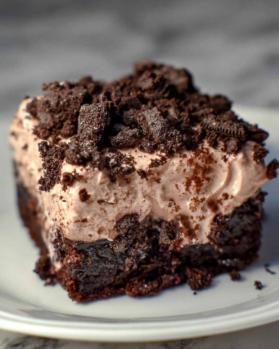 A single square piece of chocolate dessert is shown close up on a white plate with a white marbled background. The bottom layer is a dense, moist dark brown chocolate cake with a shiny, slightly gooey texture. The top layer is a thick, light brown chocolate mousse that looks creamy and fluffy, spread unevenly over the cake. There are crushed dark chocolate cookie pieces sprinkled generously on top and some sticking to the sides of the mousse. The dessert looks rich and moist. photo taken with an iphone --ar 4:5 --v 7