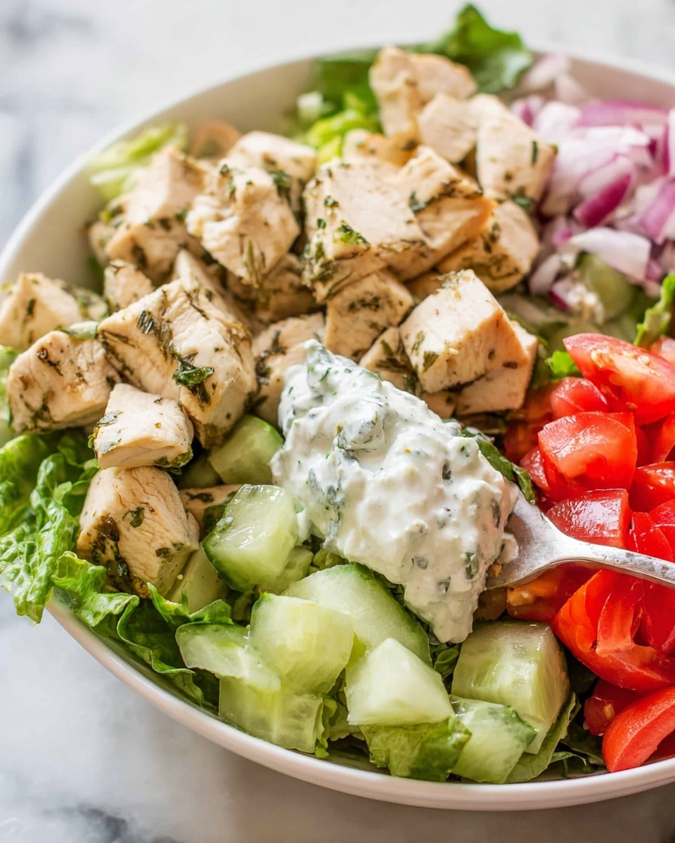 A white bowl filled with a fresh salad is placed on a white marbled surface. The bottom layer is bright green lettuce leaves covering the bowl. On the left side, there is a mix of chopped red tomatoes and small white cheese cubes. Next to the tomatoes, there are small slices of green cucumber. The top layer on the right side shows medium-sized chunks of cooked chicken with green herbs visible on the surface, giving a seasoned look. A spoon with white yogurt sauce is resting on the edge of the bowl, close to the cucumbers. The image captures the details and colors vividly, showing a fresh and healthy dish. photo taken with an iphone --ar 4:5 --v 7
