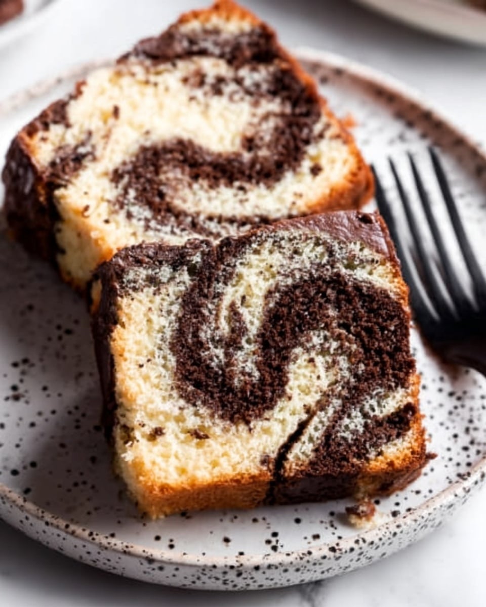 Two slices of marble cake with swirls of dark chocolate and light vanilla layers are placed closely on a white plate with black speckles. The texture of the cake looks soft and moist, with the chocolate marbling creating an artistic pattern in each slice. A black fork rests on the plate near the cake slices. The background is a white marbled surface. photo taken with an iphone --ar 4:5 --v 7