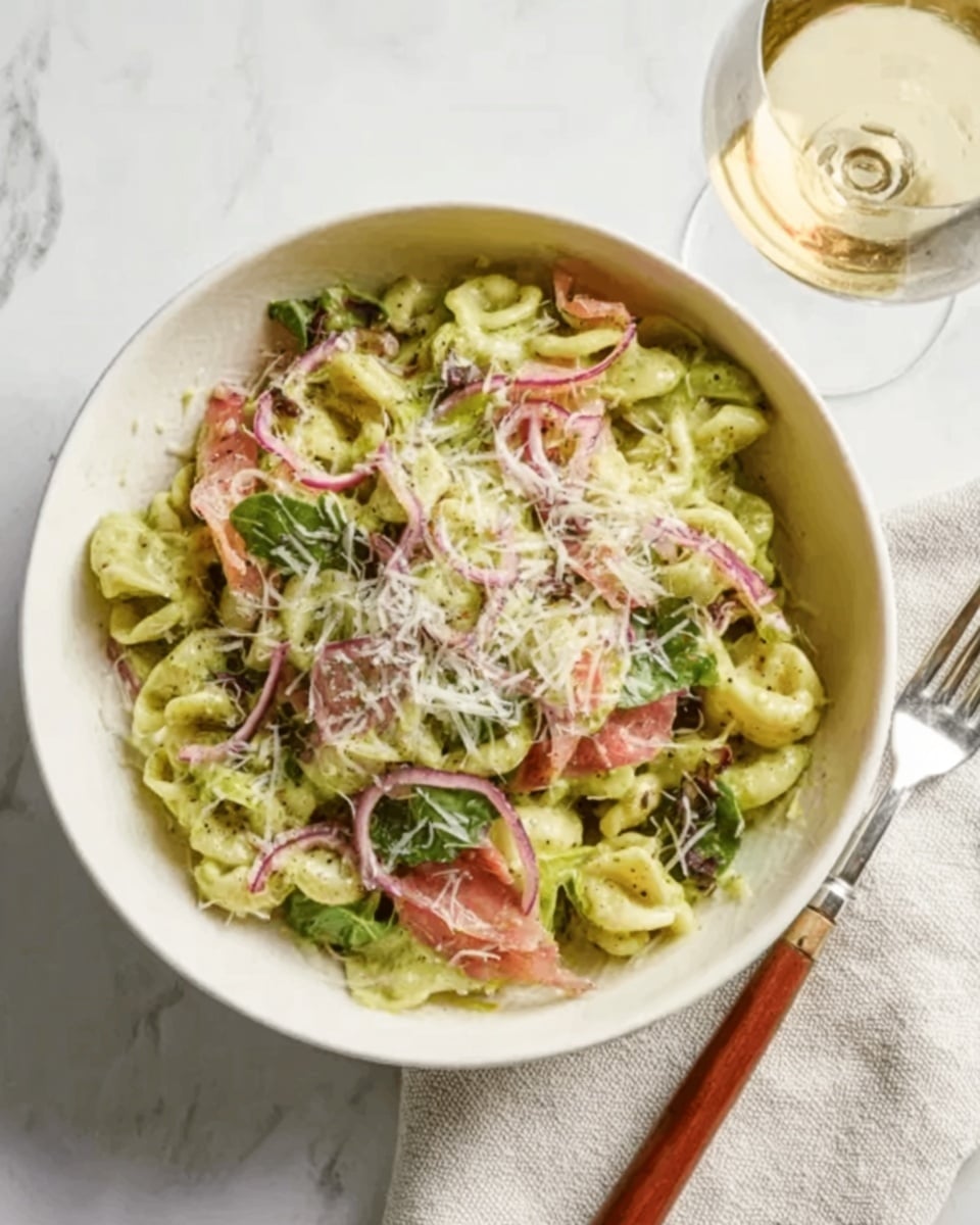 A white bowl filled with pasta that has short twisted shapes, covered in a creamy green sauce. On top, there are thin slices of pink-red pieces, thin purple onion rings, and green leaves scattered across. The dish is sprinkled with shredded white cheese. Next to the bowl is a fork with a wooden handle and a glass of white wine on a white marbled surface. Photo taken with an iphone --ar 4:5 --v 7
