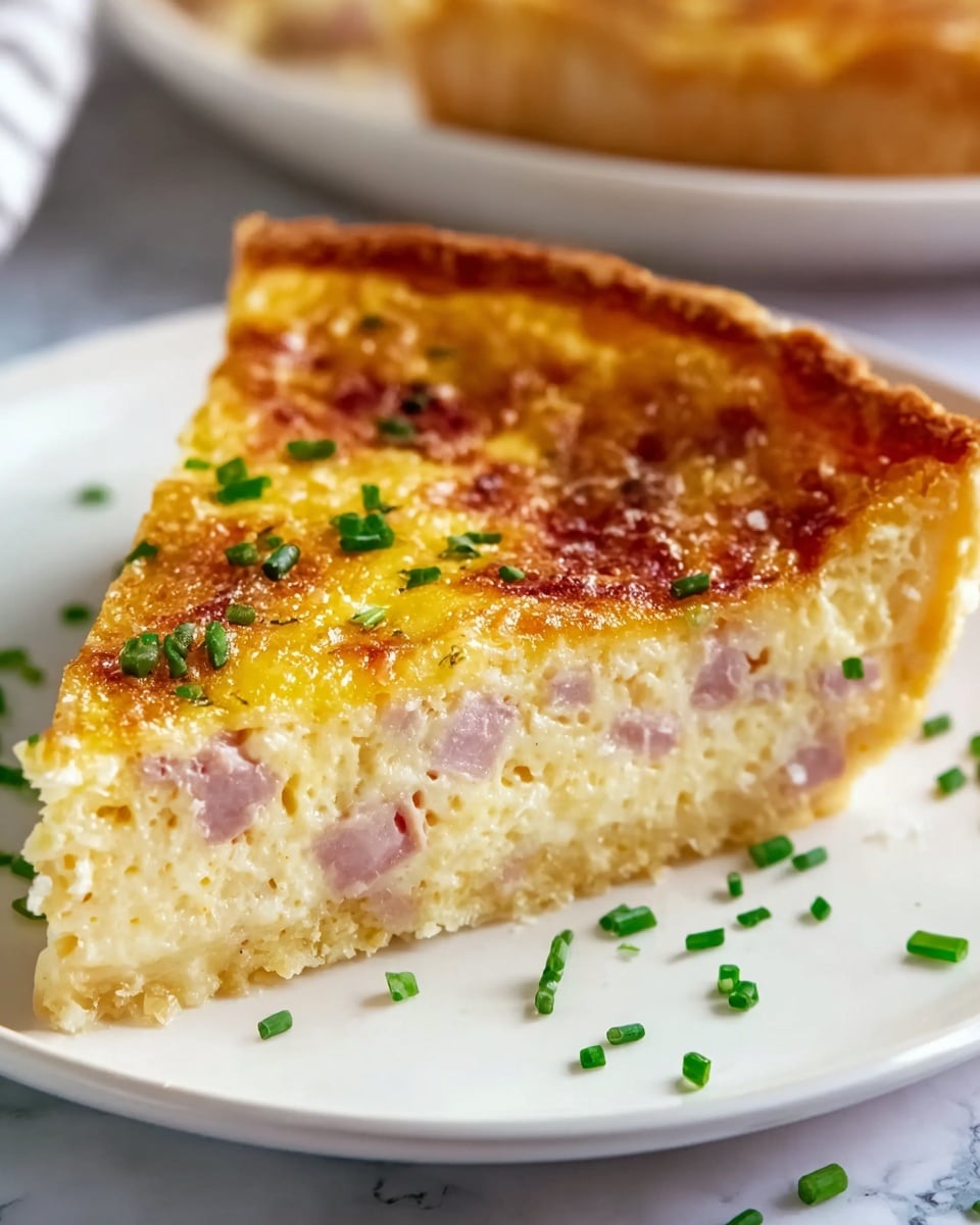 A slice of quiche is shown on a white plate with a white marbled texture surface beneath it. The quiche has three clear layers: a golden-brown, slightly crispy crust at the bottom; a thick, creamy middle layer filled with light pink ham chunks; and a smooth, golden-yellow top layer with a slightly browned, baked cheese texture. Small green chives are sprinkled on top and around the plate, adding a fresh pop of color. Photo taken with an iphone --ar 4:5 --v 7