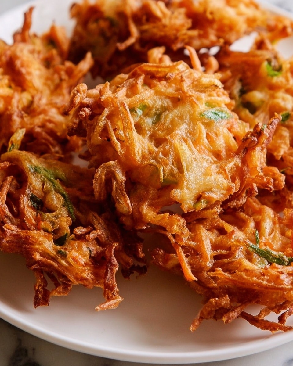 A close-up view of several crispy, golden-brown fried fritters piled on a white plate set on a white marbled surface. The fritters have an irregular shape with thin, crunchy strands and small bits of green herbs visible throughout, giving a textured and layered appearance. The outer edges are darker and crispier, while the inside looks softer and slightly orange, showing a mix of various fried vegetable pieces held together by a light batter. Photo taken with an iphone --ar 4:5 --v 7