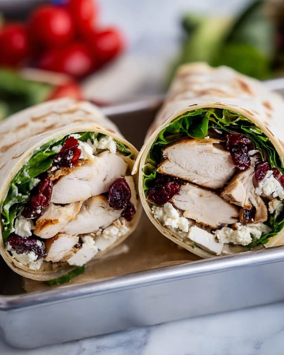 The image shows a close-up of two halves of a wrap placed side by side on a white marbled surface. Each wrap has several visible layers: the outer layer is a soft, light beige tortilla, inside which is a fresh, bright green layer of leafy lettuce. Next, large pieces of juicy, cooked chicken breast with a light brown sear are packed in, interspersed with dollops of crumbly white cheese and dark red dried cranberries, creating a mix of textures and colors. The wraps are cut to show the cross-section clearly, with the ingredients tightly packed inside. Photo taken with an iphone --ar 4:5 --v 7