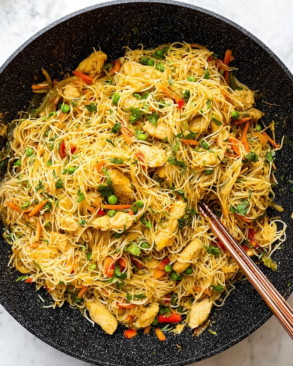 A large black non-stick pan filled with a mix of thin, golden-brown rice noodles tangled with bright orange thin carrot strips, light yellow cooked chicken pieces, and small green herbs scattered on top. The noodles and chicken are mixed with chopped green onions and tiny red bell pepper bits, adding pops of fresh green and red color. A pair of copper-colored chopsticks rests on the right side inside the pan, partly buried in the noodles. The pan is set on a white marbled surface with a clean, bright look. photo taken with an iphone --ar 4:5 --v 7