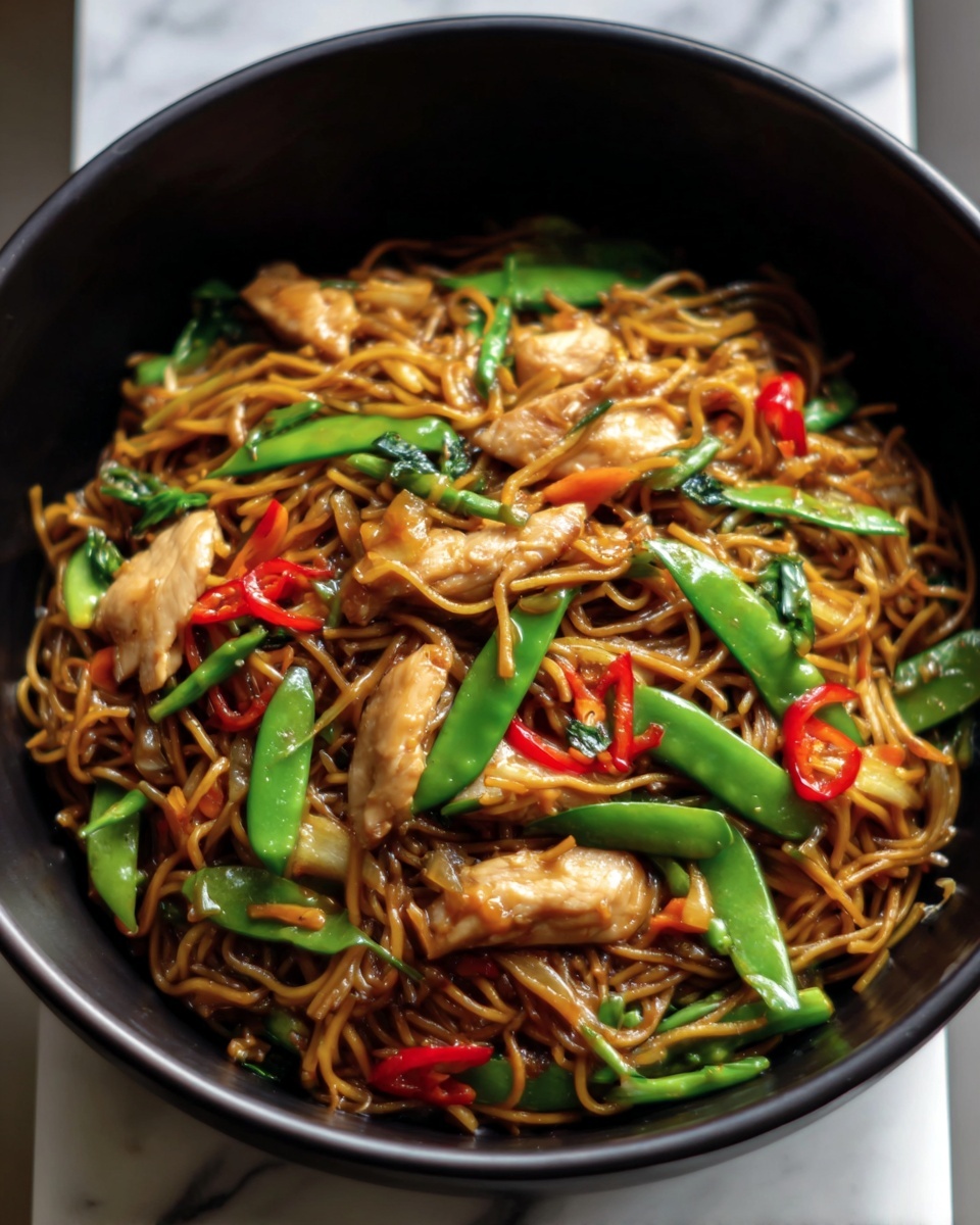 A black bowl filled with stir-fried noodles layered with chunks of cooked chicken and bright green snap peas mixed evenly throughout. Thin slices of red chili peppers are scattered on top, adding pops of color among the golden brown noodles coated in a glossy sauce. The chicken pieces look tender and juicy, while the vegetables add fresh, crisp texture to the dish. The background is a white marbled texture. photo taken with an iphone --ar 4:5 --v 7