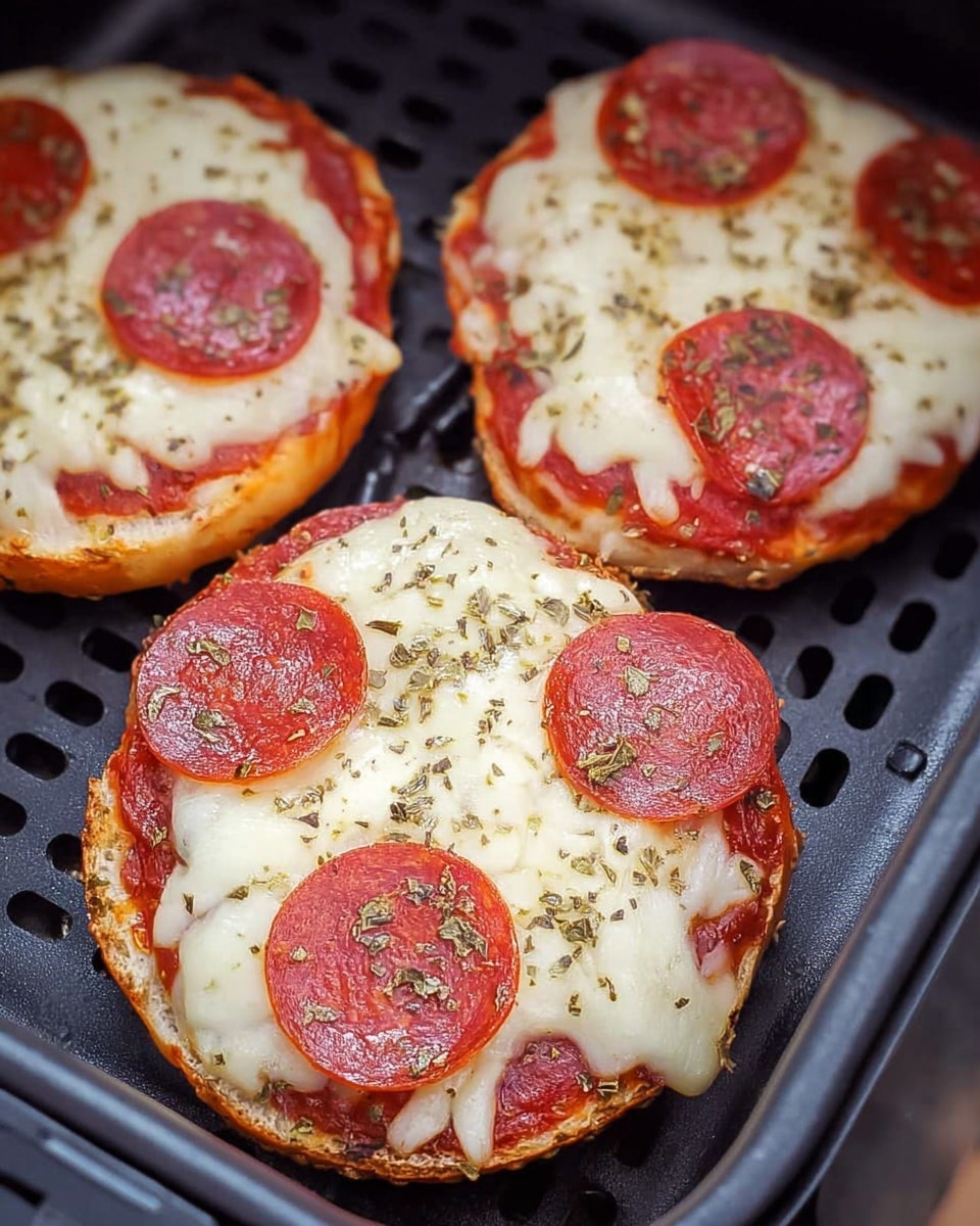 Three small pepperoni pizzas are shown on a black perforated baking tray. Each pizza has three layers: a golden-brown bread base, a bright red tomato sauce spread evenly on top, and a thick layer of melted white cheese covering the sauce. On top of the cheese, there are three slices of round, reddish-brown pepperoni on each pizza. The pizzas are sprinkled with greenish dried herbs, giving slight texture to the smooth cheese. The pizzas are arranged close to each other, with one having a noticeable hole in the center like a bagel. The overall scene sits on a white marbled texture. photo taken with an iphone --ar 4:5 --v 7