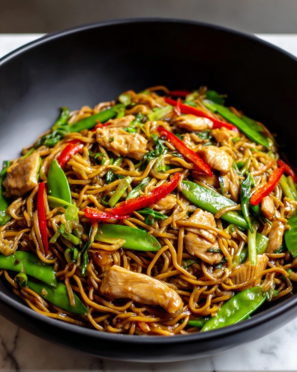 A black bowl filled with a colorful noodle dish is shown. The dish has three visible layers: at the bottom are brown thin noodles with a glossy texture, topped with sautéed pieces of light brown chicken, and scattered throughout are bright green snap peas and slices of shiny red chili peppers. The ingredients are mixed but clearly separate by color and texture, making the dish vibrant and fresh. The bowl sits on a white marbled surface. Photo taken with an iphone --ar 4:5 --v 7