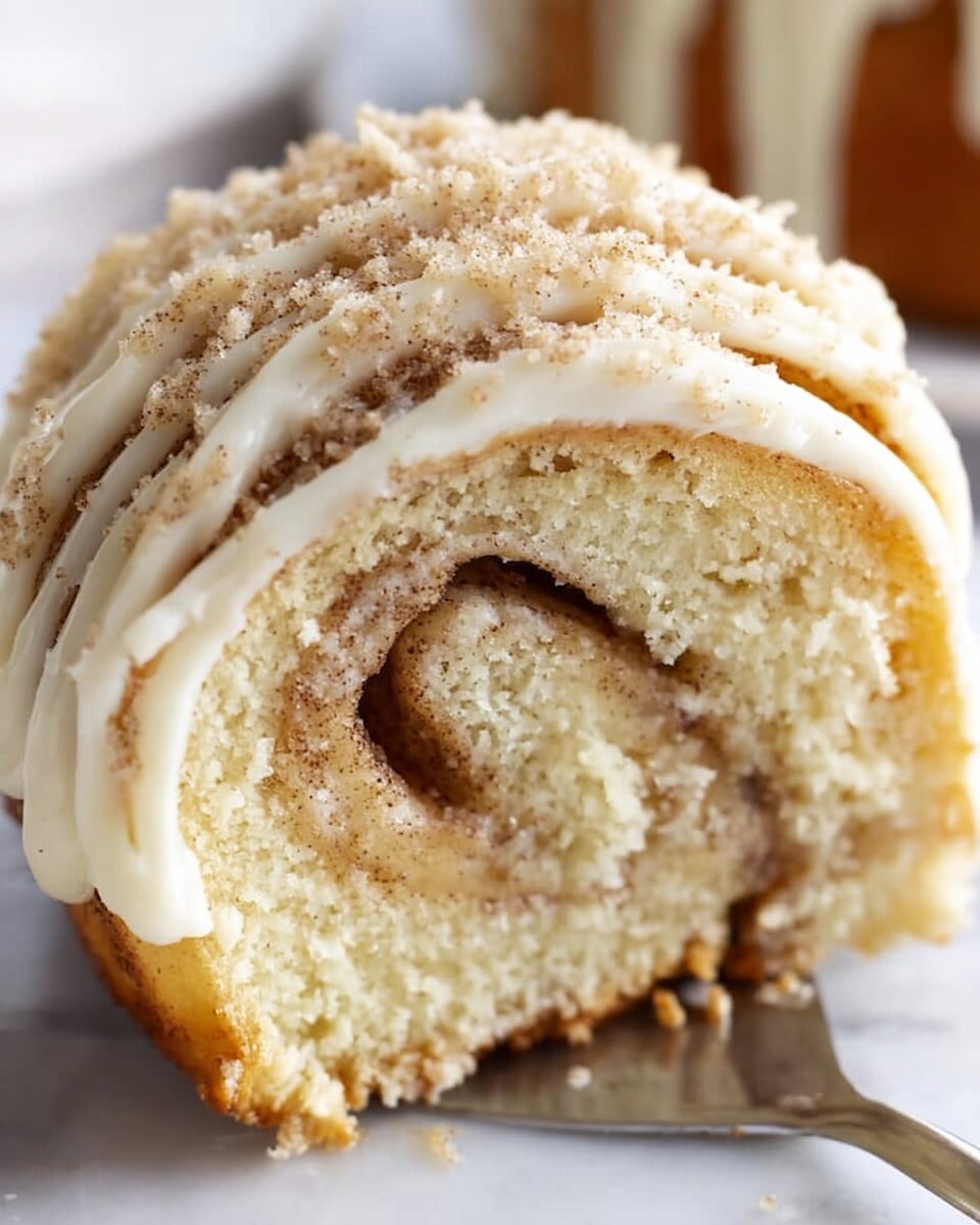 A close-up image of a cinnamon roll slice with visible layers showing a swirl of light brown cinnamon filling inside soft tan dough. The top layer is covered in thick, creamy white icing that is piped in lines across the roll, along with a sprinkling of light brown cinnamon sugar crumbs. The roll sits on a white marbled surface, and part of a metal spatula is visible holding the roll slice from below. The texture of the dough looks soft and fluffy, with a slightly golden-brown crust on the outer edge. Photo taken with an iphone --ar 4:5 --v 7