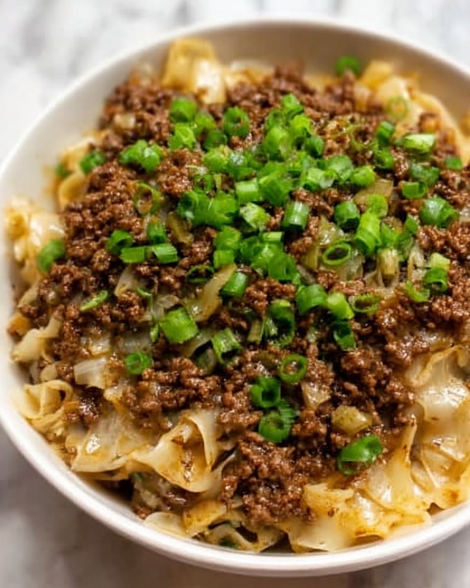 The image shows a dish with two main layers in a white bowl on a white marbled surface. The bottom layer is soft noodles, light yellow in color, slightly glossy and folded unevenly. The top layer covers the noodles with cooked ground beef, brown with small bits and mixed with diced onions, which are light and translucent. The dish is garnished with a generous amount of chopped green onions, which add a fresh green color on top. photo taken with an iphone --ar 4:5 --v 7