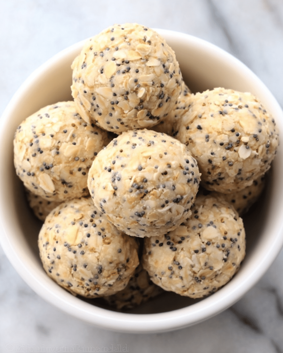 The image shows a white bowl filled with round, light beige balls speckled with small black seeds and oats, giving them a textured look. The balls are slightly rough with visible oats embedded throughout, stacked closely together inside the bowl. The background is a white marbled surface, creating a clean and simple look. photo taken with an iphone --ar 4:5 --v 7