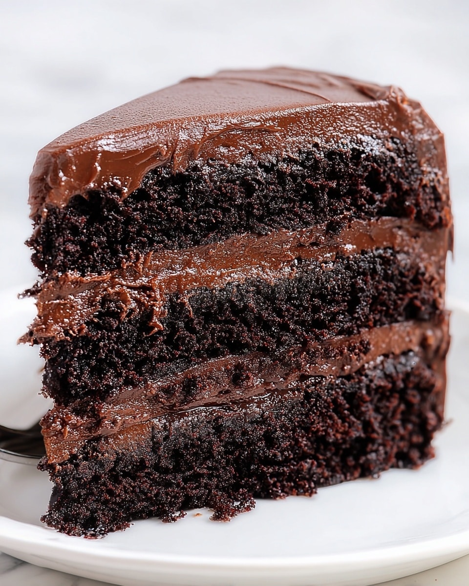 The image shows a close-up of a thick, four-layer slice of chocolate cake. Each dark, moist cake layer is separated by smooth, shiny milk chocolate frosting. The entire top of the cake is covered with a thick layer of the same glossy chocolate frosting, applied with soft, visible swirls. The cake sits on a simple white plate, set against a white marbled texture background that highlights the rich, dark brown colors of the cake and frosting. photo taken with an iphone --ar 4:5 --v 7