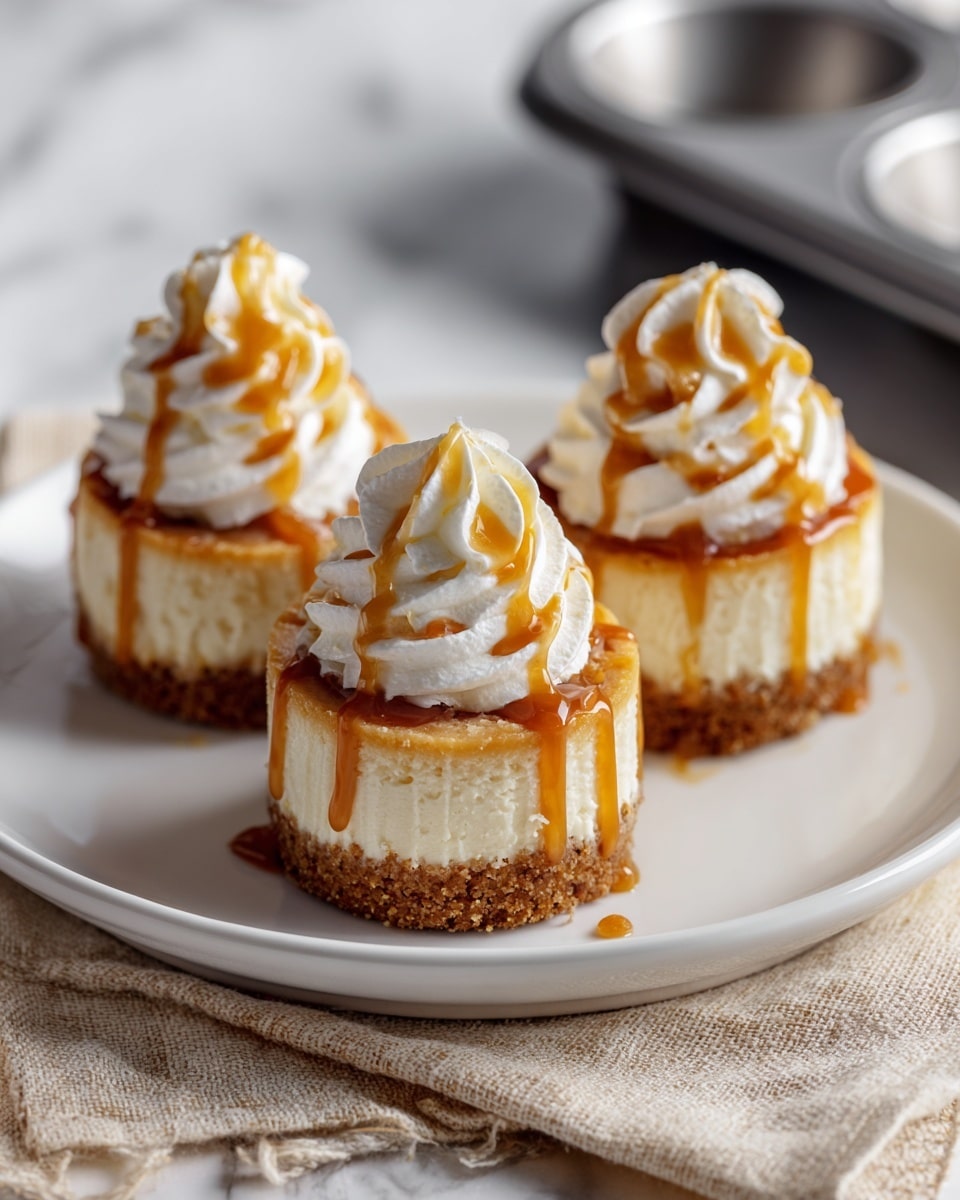 Three mini cheesecakes are placed on a white plate on top of a beige cloth on a white marbled surface. Each cheesecake has three layers: a crumbly brown base, a thick white creamy middle, and a thin golden caramel glaze on top. A tall swirl of white whipped cream sits on each cheesecake, with caramel sauce drizzled over the whipped cream and running down the sides. The background is softly blurred with a dark muffin tray and a white cloth visible. Photo taken with an iphone --ar 4:5 --v 7