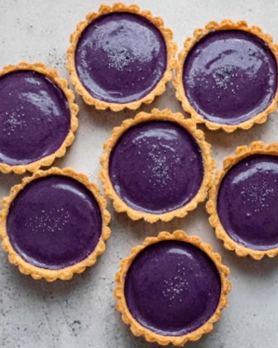 The image shows six small tartlets arranged closely together on a white marbled surface. Each tartlet has a golden-brown crust that holds a smooth, shiny filling in deep purple color, almost like a rich blueberry or ube flavor. The filling is even and reflective, contrasting well with the crisp edge of the crust. The tartlets are filled to the brim with no visible cracks or toppings, keeping the surface clean and glossy. photo taken with an iphone --ar 4:5 --v 7