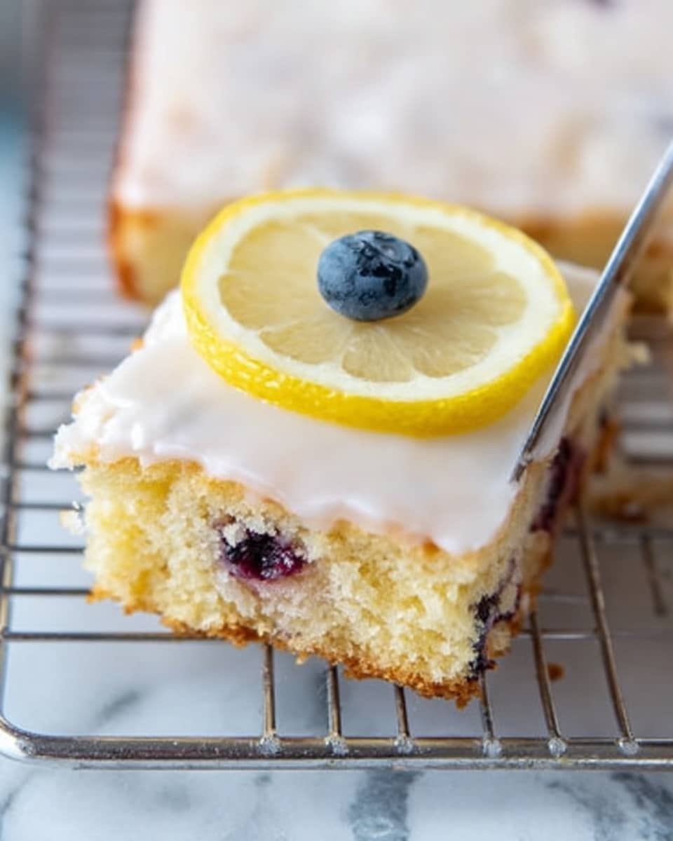 A square piece of cake with a smooth white icing layer covers the top, slightly dripping over the edges. The cake inside shows a light yellow color with bits of blueberries visible throughout. On top, a small yellow lemon slice is placed next to a single plump blueberry, both resting near the edge. The cake sits on a white cooling rack, which is placed over a white marbled surface. A knife with some icing residue is in the background. photo taken with an iphone --ar 4:5 --v 7