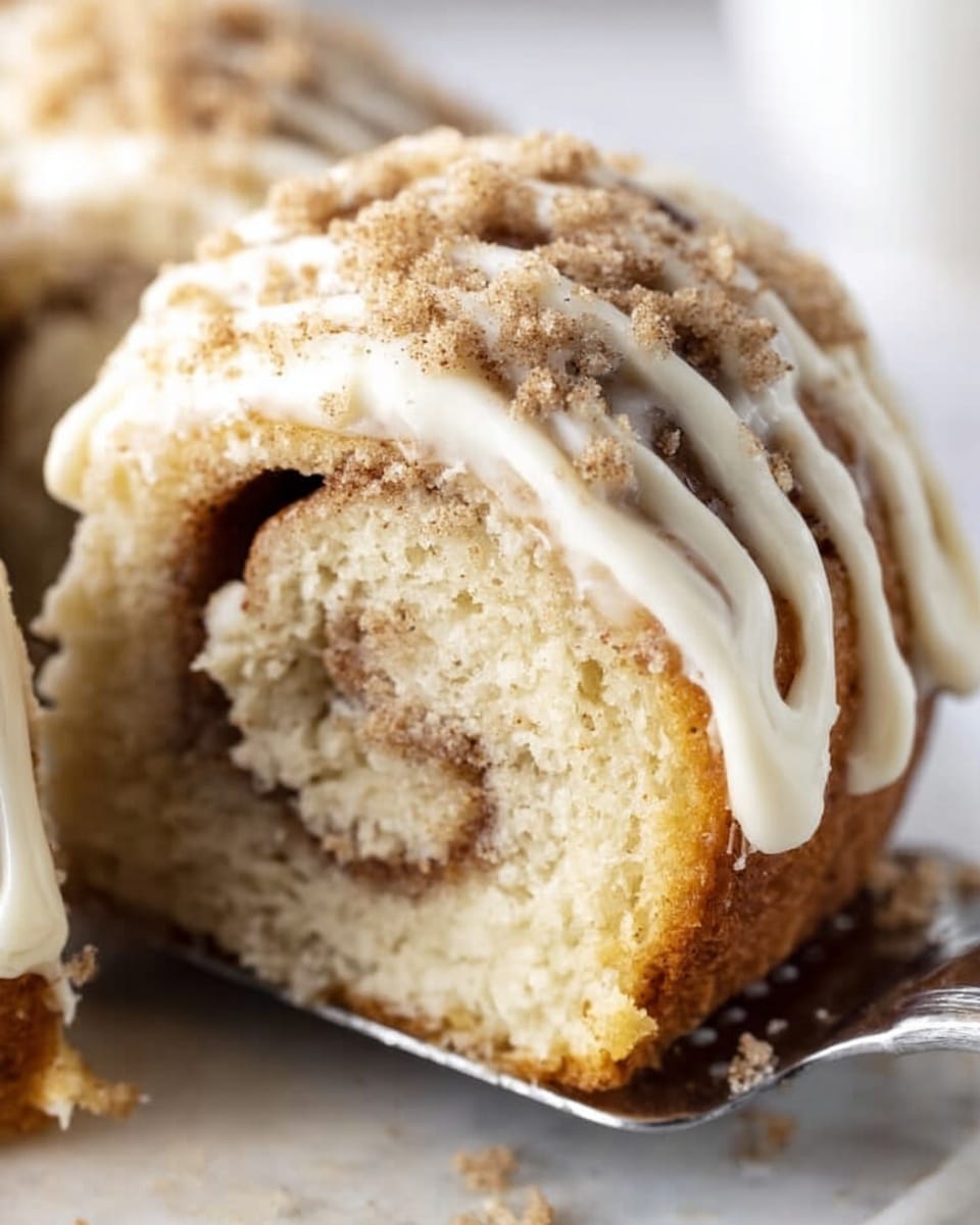 The image shows a close-up of a cinnamon roll cake slice with three visible layers: a soft light brown outer cake layer, a slightly darker swirl of cinnamon sugar filling inside, and a thick white glaze drizzled over the top in stripes. The glaze is creamy and smooth with a light dusting of brown sugar or cinnamon powder sprinkled on top. The cake sits on a white marbled surface, and a woman's hand is holding a utensil underneath the slice to lift it. Photo taken with an iphone --ar 4:5 --v 7