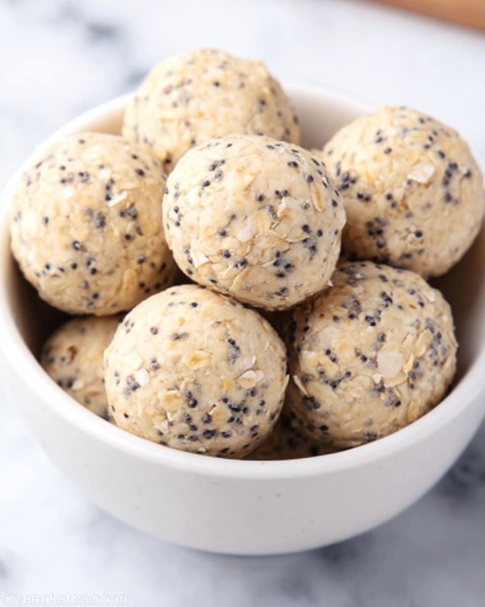 The image shows a white bowl filled with round, beige-colored snacks speckled with small black seeds. Each ball has a slightly rough texture and appears soft but firm, with streaks and tiny pieces visible within the dough. The balls are piled loosely in the bowl, sitting on a white marbled surface. The lighting is bright and natural, highlighting the texture and details of the snacks. photo taken with an iphone --ar 4:5 --v 7